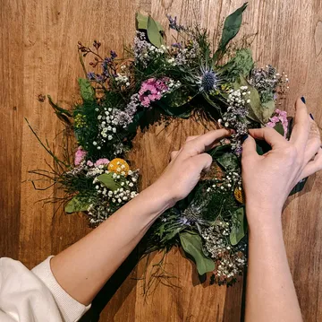 Hands arranging a floral wreath on wood.