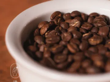 Coffee beans lie in a bowl on a table.