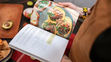 Person holding cookbook with taco recipe.