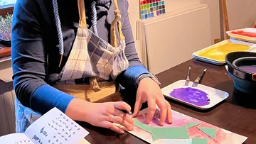 Person, die am Tisch mit farbigem Papier bastelt.