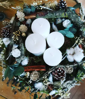 Kerzen, umgeben von Tannenzapfen und viel Grün.
