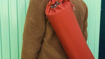 Person carrying a red yoga mat bag outdoors.