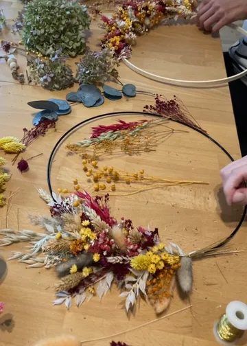 Person, die auf dem Tisch einen Kranz mit getrockneten Blumen bastelt.
