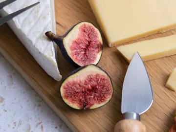 Figs and cheese on a wooden board with a knife.