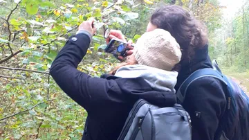Zwei Wanderer untersuchen Pflanzen im Wald mit einer Lupe.
