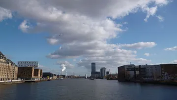 Fluss mit Gebäuden unter bewölktem Himmel.
