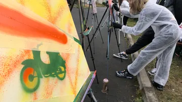 Person spray paints motorcycle stencil on canvas.