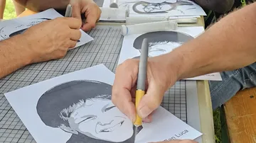Hands drawing on paper portraits at table.