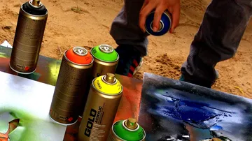 Person, die Kunst mit Dosen auf Sand sprüht.