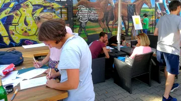 Leute, die draußen in der Nähe eines farbenfrohen Wandgemäldes zeichnen.