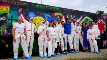 Group wearing protective suits in front of graffiti wall.