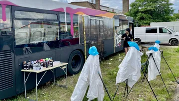 Colorful bus with spray paint setup outdoors.