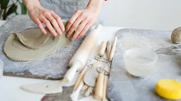 Hands shaping clay on a pottery workspace.
