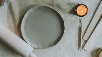 Clay plate with candle and tools on table.