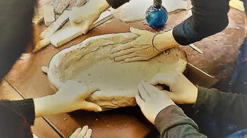Hands shaping clay bowl on table.