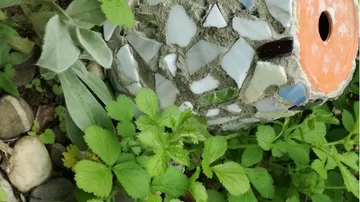 Mosaic-decorated garden birdhouse surrounded by plants.