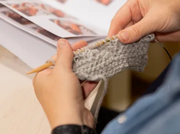 Handstricken mit grauem Garn, Musterheft in der Nähe.