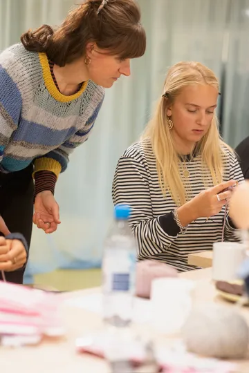 Two women engaged in a knitting activity indoors.