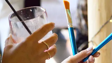 Person, die im Haus Pinsel und Plastikbecher in der Hand hält.