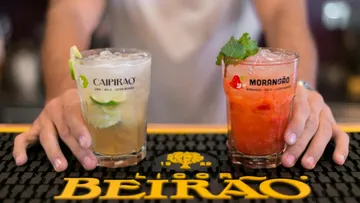 Two cocktails on a bar, held by person.