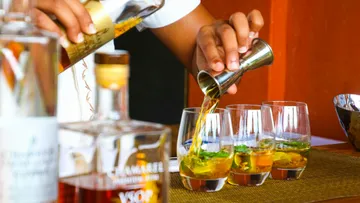 Bartender pouring drinks into glasses on bar.