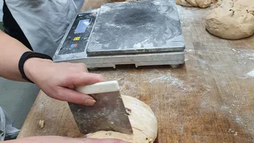 Person, die Teig mit einem Schaber auf dem Tisch schneidet.