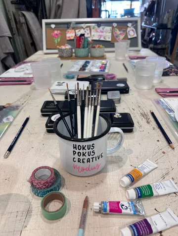Pinsel im Becher auf dem Kunsttisch mit Zubehör.