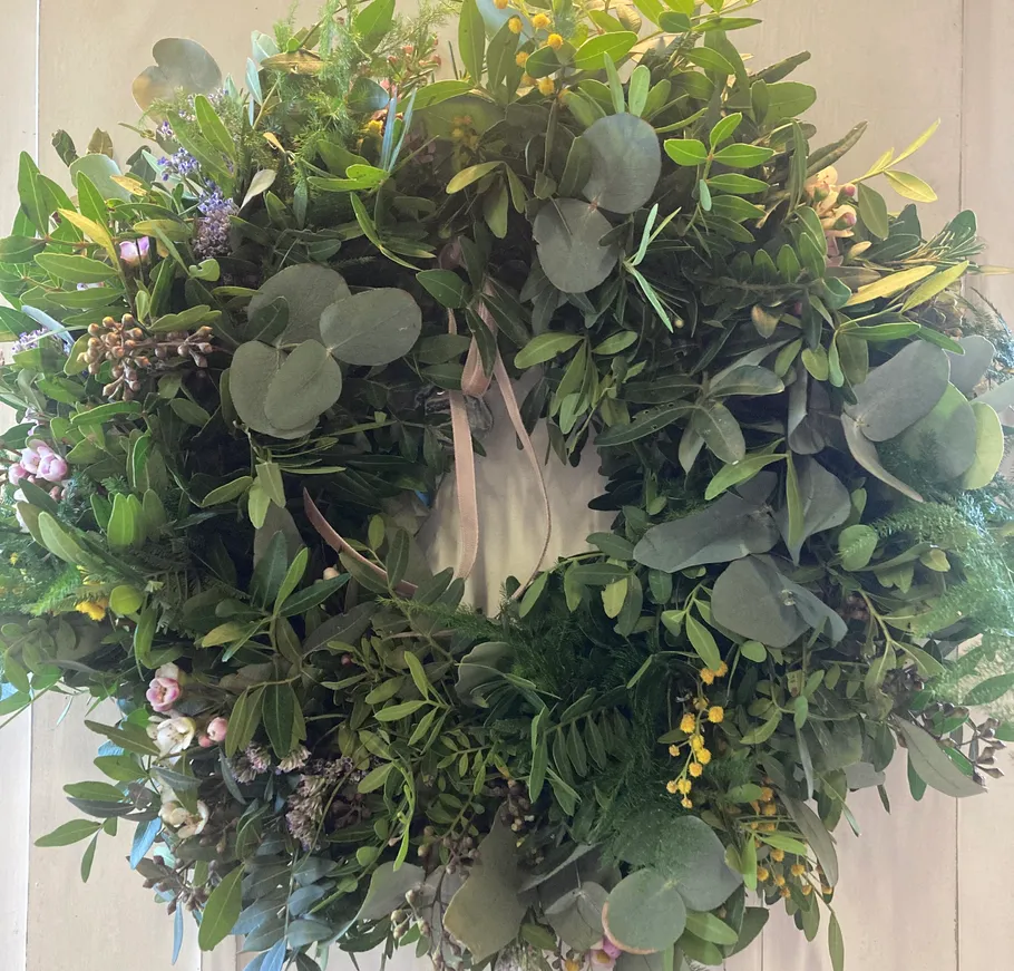 Grüner Kranz mit rosa Blumen an der Wand.