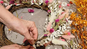 Hands crafting a floral wreath with pink and white flowers.