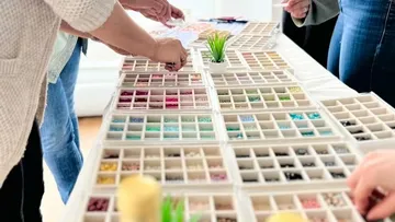 People selecting beads from organized trays on table.