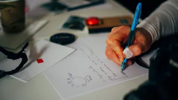 Person, die am Schreibtisch Notizen auf Papier schreibt.