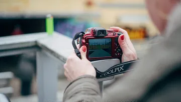Person holding red camera taking photo outdoors.
