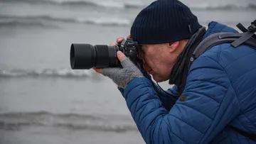 Person photographing beach with camera and telephoto lens.
