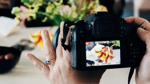 Hände, die eine Kamera halten, um ein Blumenarrangement einzufangen.