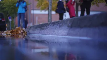 People walk on wet pavement beside curb.