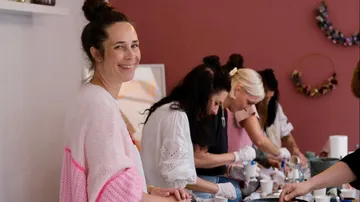Woman smiling, others crafting at a table.