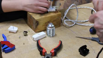 Hands assembling light fixture on workbench.