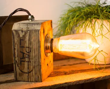 Wooden lamp with exposed Edison bulb, plant nearby.