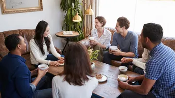 Group of six people sitting and talking in living room.