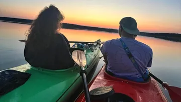 Zwei Personen beim Kajakfahren bei Sonnenuntergang auf ruhigem Wasser.
