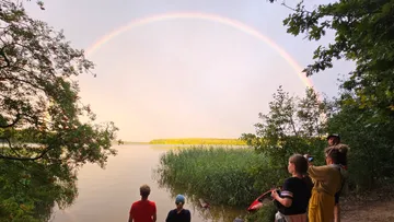 Menschen am See mit einem Regenbogen über dem Kopf.