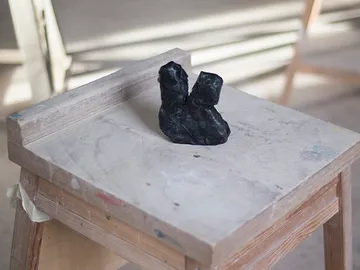 Black object stands on a wooden chair in a studio.