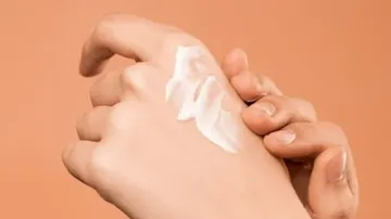 Hands applying cream on skin, orange background.