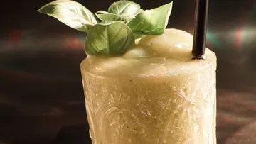 Gefrorener Cocktail mit Basilikumgarnitur und Stroh.