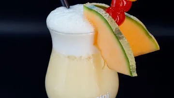 Creamy cocktail with melon and cherry garnish.