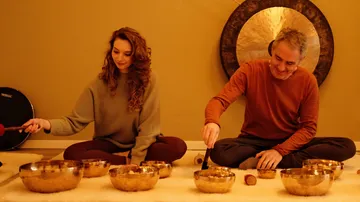 Two people playing singing bowls indoors.