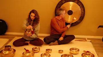 Two people playing a gong and sound bowls.