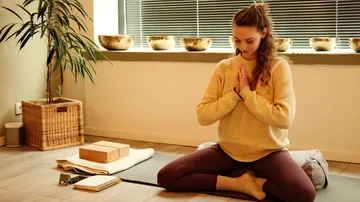 Frau meditiert drinnen auf einer Yogamatte.