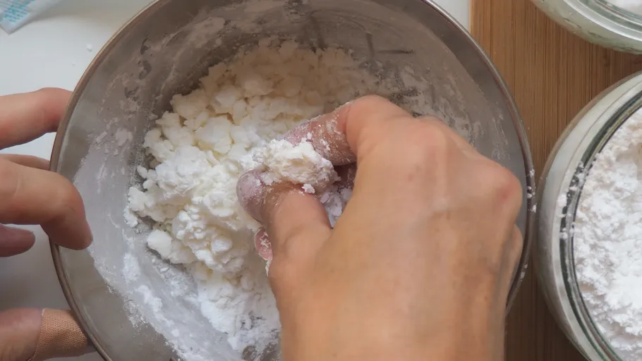 Hands mixing dough in a metal bowl.