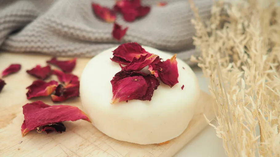 White soap with red petals on wooden board.